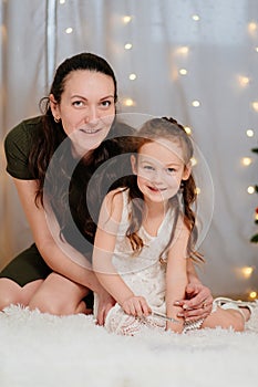 mother with little daughter sit on the floor against the background of a garland