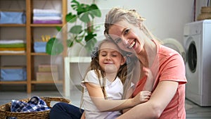 Mother and little daughter sit on floor and look at camera, family smile and laugh. Girl hug