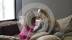 Mother and little daughter are sitting on the bed and smacking