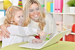 Mother with little daughter using modern laptop