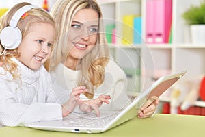 Mother with little daughter using modern laptop at home