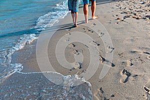 Mother with little daughter walk on beach leaving footprints in sand