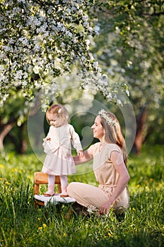 Mother and little daughter walk in blooming apple garden.