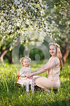 Mother and little daughter walk in blooming apple garden.