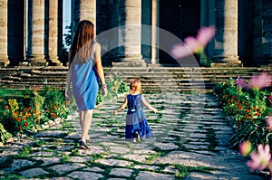 Mother with little daughter walk on stone path towards old temple