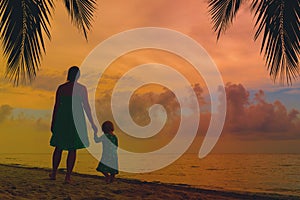 mother and little daughter walking on beach at sunset