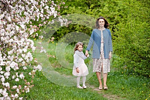 Mother and little daughter walking in blooming apple garden. Mom loves her child. Spring story. Happy family in beautiful spring