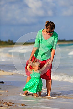 Mother and little daughter walking on summer beach