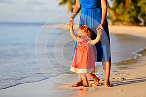 Mother and little daughter walking on summer beach