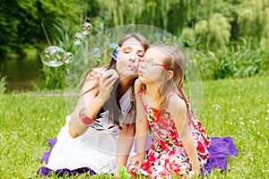 Mother and little girl blowing soap bubbles in park.