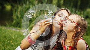 Mother and little girl blowing soap bubbles in park.