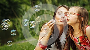 Mother and little girl blowing soap bubbles in park.