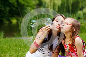 Mother and little girl blowing soap bubbles in park.