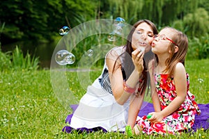 Mother and little girl blowing soap bubbles in park.