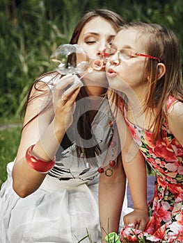 Mother and little girl blowing soap bubbles in park.