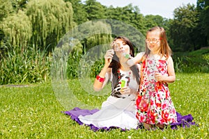 Mother and little girl blowing soap bubbles in park.