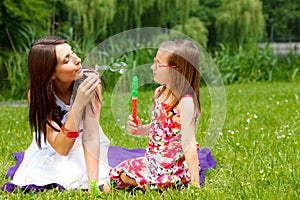 Mother and little girl blowing soap bubbles in park.