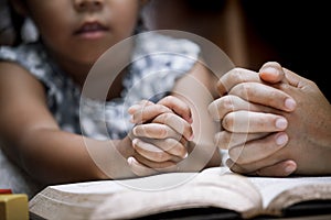 Mother and little girl hands folded in prayer on a Holy Bible