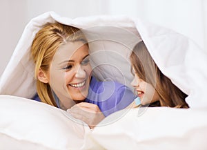 Mother and little girl under blanket at home