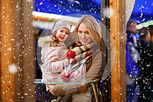 Mother and little kid girl eating crystalized apple on Christmas