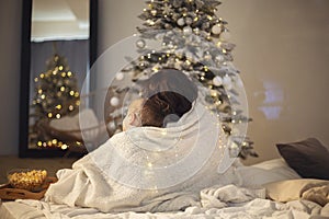 Mother with little kid watch Christmas movies at home during winter holidays, sitting near xmas tree