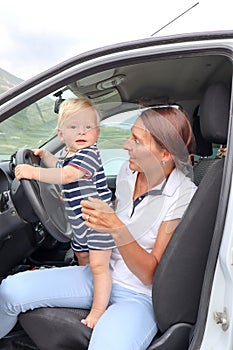 Mother and little son infant are sitting in the driver`s seat in carwith mountains on background