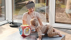Mother and little son laughing and playing educational toys sitting on floor at home