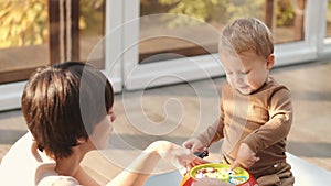 Mother and little son laughing and playing educational toys sitting on floor at home