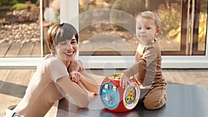 Mother and little son laughing and playing educational toys sitting on floor at home