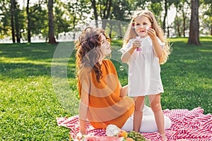 Mother looking her daughter blowing sopa bubbles in the park photo