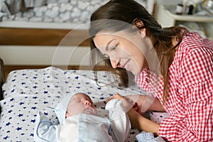 Mother looks at her child. Young mother looking on her newborn baby. Beautiful mom lying at bed with a cute sleeping new born