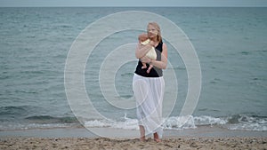 Mother with lost look holding baby being alone at the beach near sea