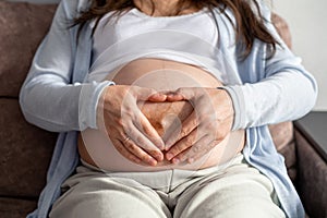 Mother love. pregnant woman with big belly advanced pregnancy resting sitting on sofa at home making heart hands