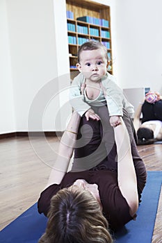 Mother lying on back and holding her baby during a yoga class