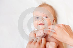 Mother makes baby massage with happy newborn at white bed