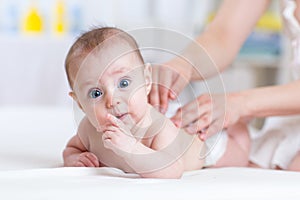 Mother massaging baby infant in bed at home