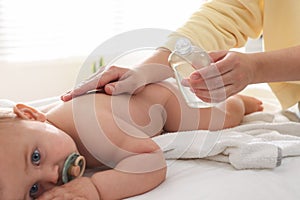 Mother massaging her cute baby with oil on bed at home, closeup