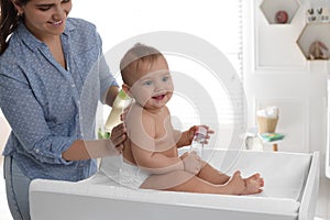 Mother massaging her cute baby with oil on changing table at home