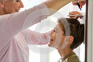 Mother measuring the height of her son against wall