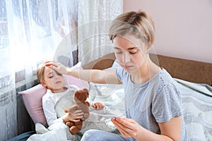 Mother measuring temperature of her ill child. Sick child with high fever laying in bed with teddybear. Fever Concept