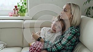 Mother measuring temperature of her ill kid at background. Sick child with high fever lying at sofa at home