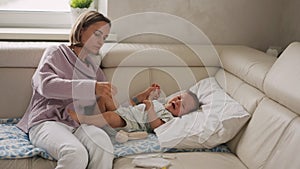 Mother measuring temperature of her ill kid at background. Sick child with high fever lying at sofa at home.