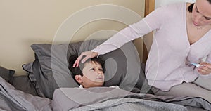 Mother measuring temperature of her ill kid and giving cup of milk in bed