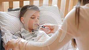 Mother measuring temperature of her ill kid. Sick child with high fever lying at bad at home