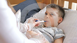 Mother measuring temperature of her ill kid. Sick child with high fever lying at bad at home