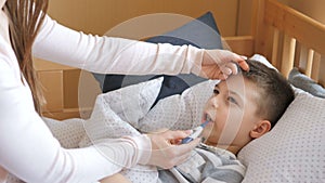 Mother measuring temperature of her ill kid. Sick child with high fever lying at bad at home