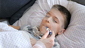 Mother measuring temperature of her ill kid. Sick child with high fever lying at bad at home