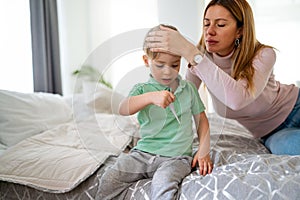 Mother measuring temperature of her ill kid. Sick child with high fever, mother holding thermometer.