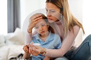 Mother measuring temperature of her ill kid. Sick child with high fever, mother holding thermometer.