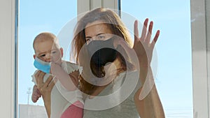 Mother in medical mask communicated with baby on hands through glass window. Covid-19 pandemic sick people in quarantine